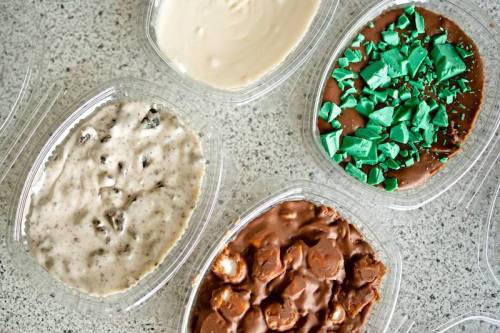 Four containers of dessert: one with creamy vanilla, one with cookies and cream, one with chocolate and green toppings, and one with caramel.