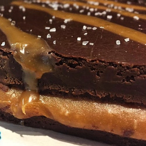 Close-up of a chocolate dessert with a gooey caramel layer, topped with a drizzle and a sprinkle of sea salt.