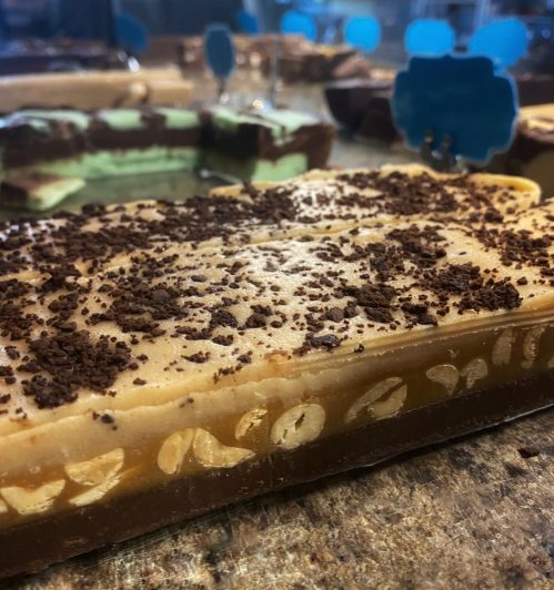 A close-up of layered dessert with chocolate and cream, topped with crushed chocolate, on a reflective surface.