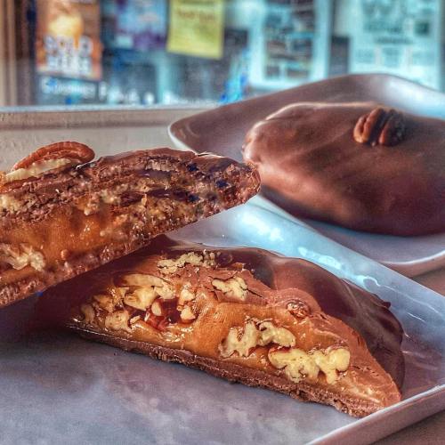 A close-up of a chocolate-covered dessert, revealing a gooey caramel and nut filling, with another dessert in the background.