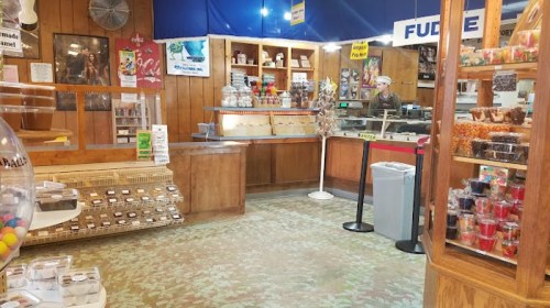 A cozy candy shop interior with wooden shelves, jars of sweets, and a counter displaying various treats.