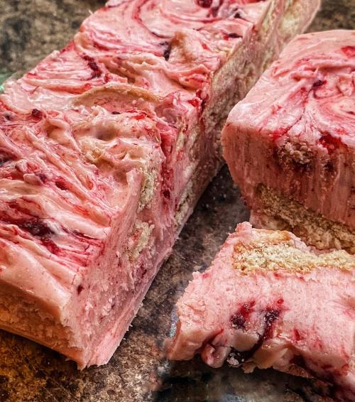 A close-up of a pink, swirled dessert with layers and a slice cut out, revealing a creamy texture and berry swirls.