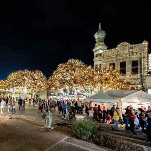 A bustling plaza at night, adorned with twinkling lights and festive decorations, with people enjoying the atmosphere.