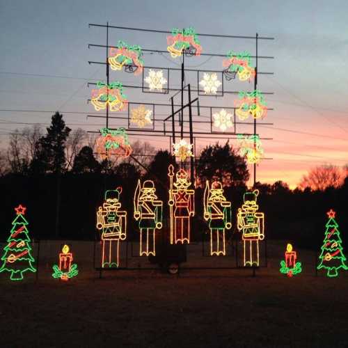 Colorful Christmas lights display featuring toy soldiers, snowflakes, and trees against a sunset sky.