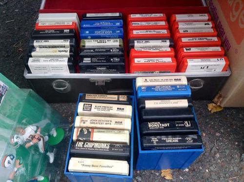 A collection of cassette tapes in a box, featuring artists like Billy Joel, Elvis Presley, and The Chipmunks.