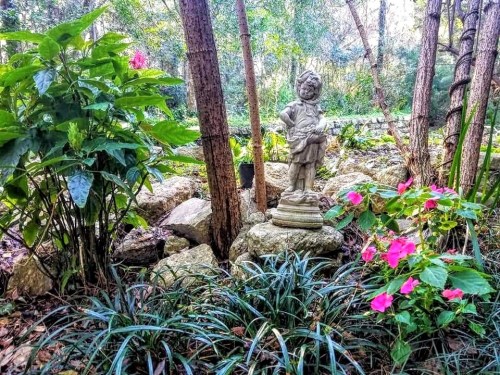 A garden scene featuring a statue of a child surrounded by lush greenery and colorful flowers.