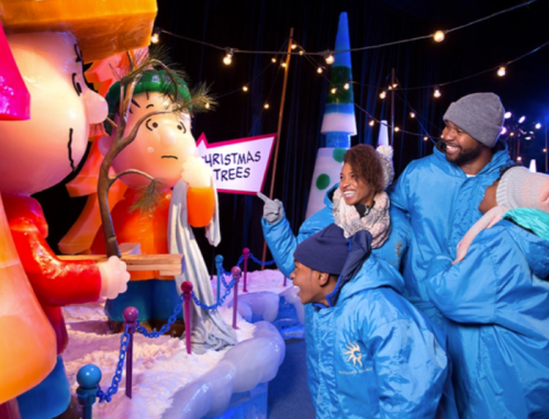 A family enjoys a festive display with ice sculptures and Christmas decorations, smiling and pointing at a character.