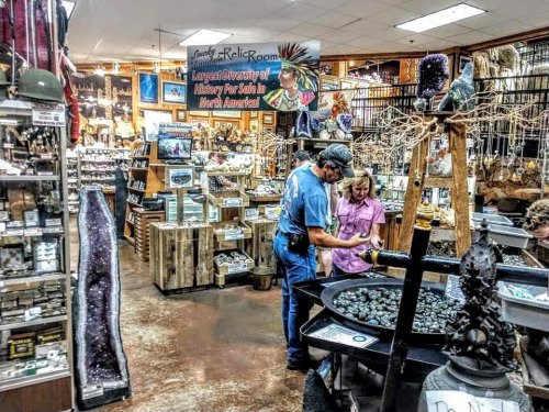 A man and a woman examine items in a vintage shop filled with various historical artifacts and collectibles.
