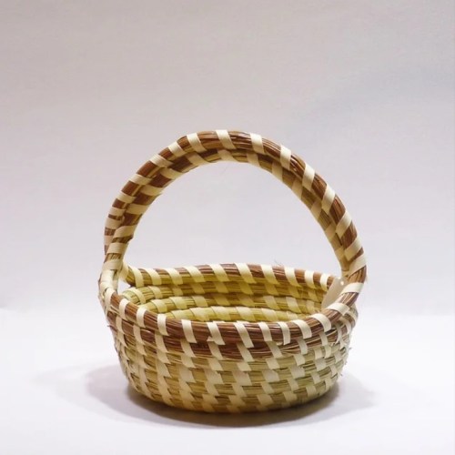 A woven basket with a handle, featuring a pattern of light and dark stripes.