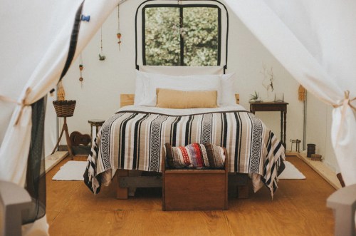 Cozy tent interior featuring a bed with a striped blanket, wooden accents, and natural light from a window.