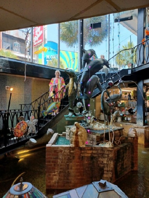 A colorful indoor space featuring sculptures of dolphins and flamingos, with a person in bright clothing on a staircase.