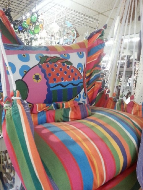 A colorful striped hanging chair with a fish-patterned pillow, displayed in a store.