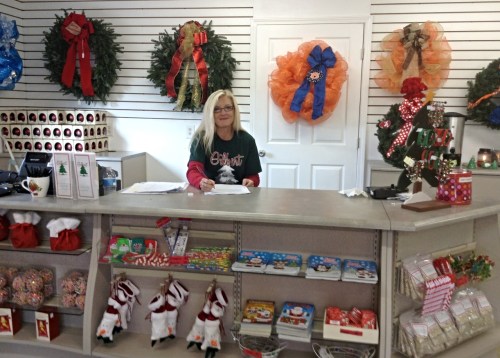 A woman sits at a counter in a festive shop, surrounded by holiday wreaths and decorations.
