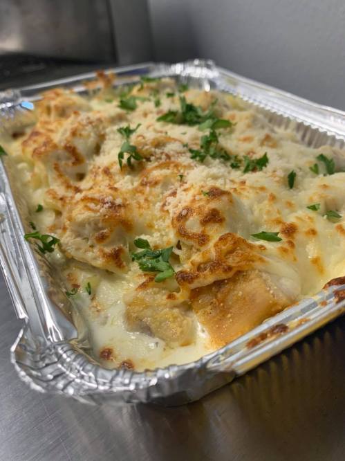 A baked dish in a foil tray, featuring creamy sauce, bread pieces, and a golden, cheesy topping, garnished with parsley.