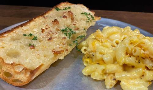 A plate with cheesy macaroni and a slice of garlic bread topped with herbs.