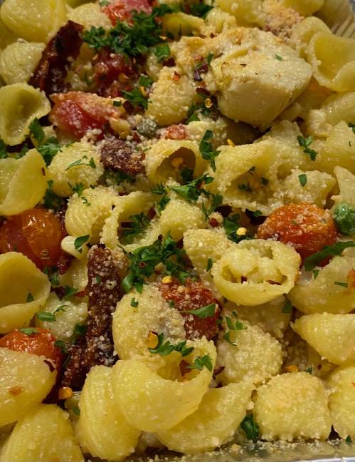 A close-up of pasta with tomatoes, herbs, and cheese, garnished with parsley and red pepper flakes.