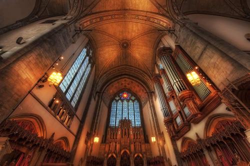 Interior of a grand church, featuring a high ceiling, stained glass windows, and a large organ. Warm lighting enhances the atmosphere.