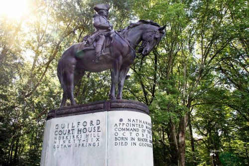 Statue of a mounted soldier at Guilford Courthouse, surrounded by trees, with an inscription detailing his history.
