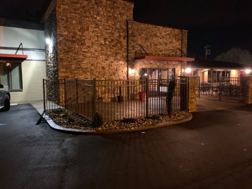 A stone building at night with a fenced entrance and outdoor seating area, illuminated by warm lights.