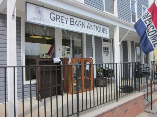 Exterior of Grey Barn Antiques shop with a welcoming sign and vintage furniture displayed on the porch.