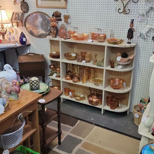 A vintage shop display featuring shelves of copper items, a wooden table, and various decorative pieces.