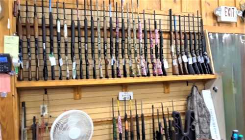 A display of various rifles hanging on a wall in a store, with tags and a fan visible in the foreground.