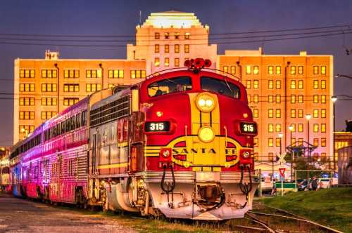 A vintage Santa Fe train parked near a brightly lit historic building at dusk.