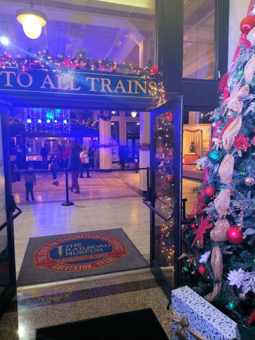 Entrance to a festive train station, decorated for the holidays with a Christmas tree and colorful lights.