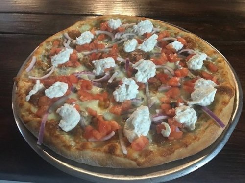 A pizza topped with diced tomatoes, red onions, and dollops of white cheese on a golden crust.