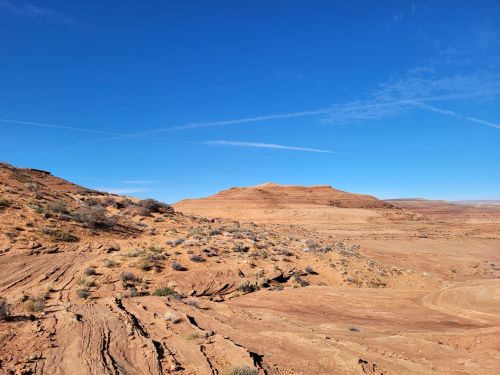 A vast desert landscape with reddish-brown hills under a clear blue sky, featuring sparse vegetation and rocky terrain.