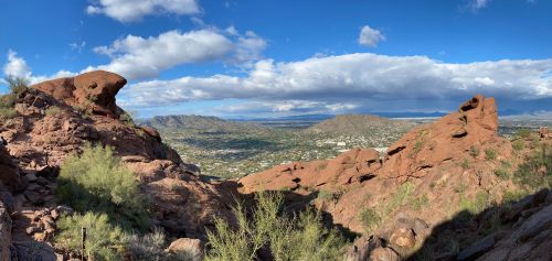 A panoramic view of rocky terrain and green valleys under a blue sky with scattered clouds.