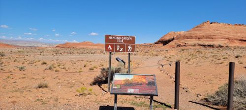 Sign for Hanging Garden Trail in a desert landscape with red rock formations and clear blue sky.
