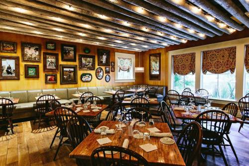 Cozy restaurant interior with wooden beams, framed art, and tables set for dining. Warm lighting creates an inviting atmosphere.