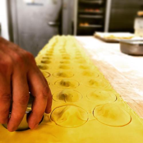 A hand using a round cutter on a sheet of pasta to create circular shapes for ravioli.