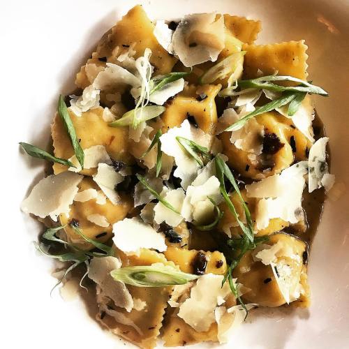 A bowl of ravioli topped with shaved cheese, green onions, and a drizzle of sauce.