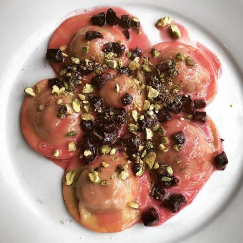 A plate of ravioli topped with a vibrant sauce, chopped beets, and crushed pistachios.