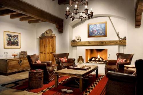 Cozy living room with a fireplace, leather chairs, a wooden table, and artwork on the walls, featuring warm lighting.