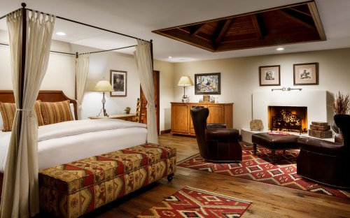 Cozy hotel room featuring a four-poster bed, fireplace, and rustic decor with warm lighting and wooden accents.