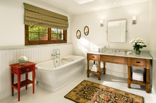 Bright bathroom featuring a freestanding tub, wooden vanity, and a window with a view, accented by a decorative rug.