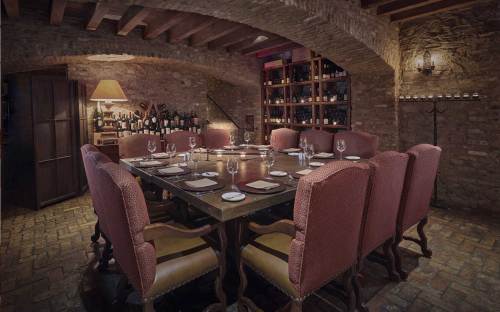 A cozy, dimly lit dining room with a large table surrounded by upholstered chairs and a wine rack in the background.