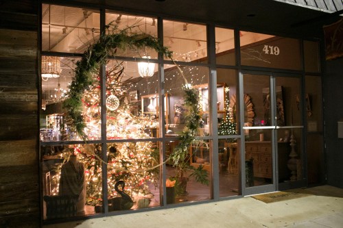 A festive storefront decorated with a Christmas tree and lights, featuring a large wreath on the window.