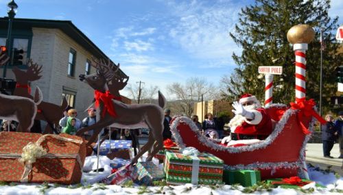 Santa Claus waves from his sleigh, surrounded by reindeer and festive gifts at a holiday parade.