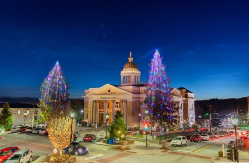 A festive courthouse adorned with colorful lights, surrounded by decorated trees, under a twilight sky.