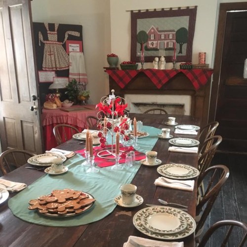 A festive dining table set with plates, candles, and holiday decorations in a cozy, rustic room.