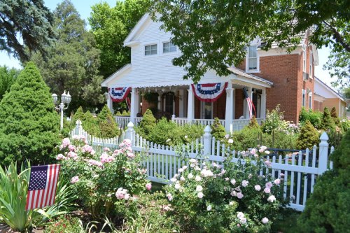 A charming house with a white picket fence, surrounded by lush greenery and blooming roses, decorated for a celebration.