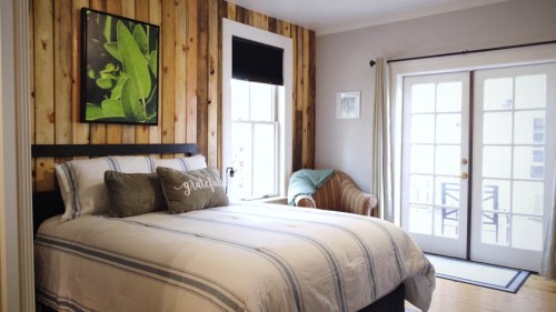 Cozy bedroom with a wooden accent wall, a bed with striped bedding, and a small seating area by the window.