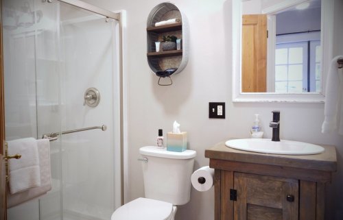 A modern bathroom featuring a shower, toilet, wooden vanity, and decorative shelf with toiletries.
