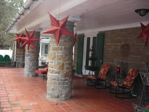A porch with stone columns, red star decorations, and cozy seating on a tiled floor.