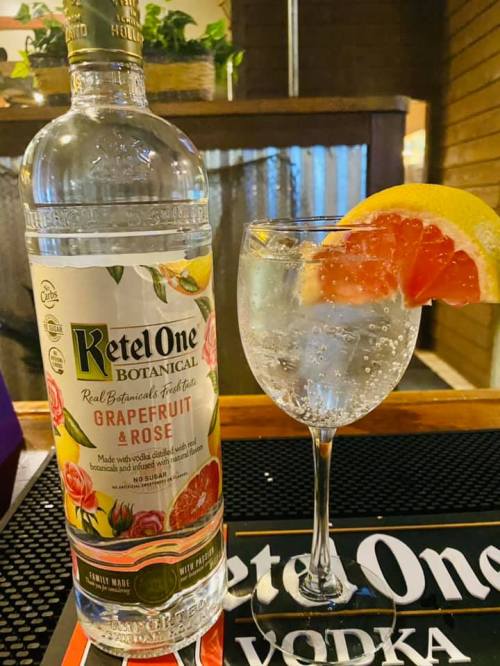A bottle of Ketel One Grapefruit & Rose vodka next to a glass of sparkling water garnished with a lemon and grapefruit slice.