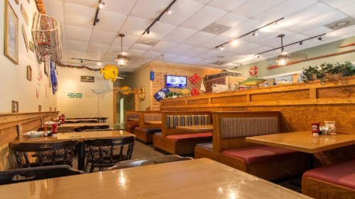 Interior of a casual restaurant with wooden booths, tables, and nautical decor, creating a cozy dining atmosphere.